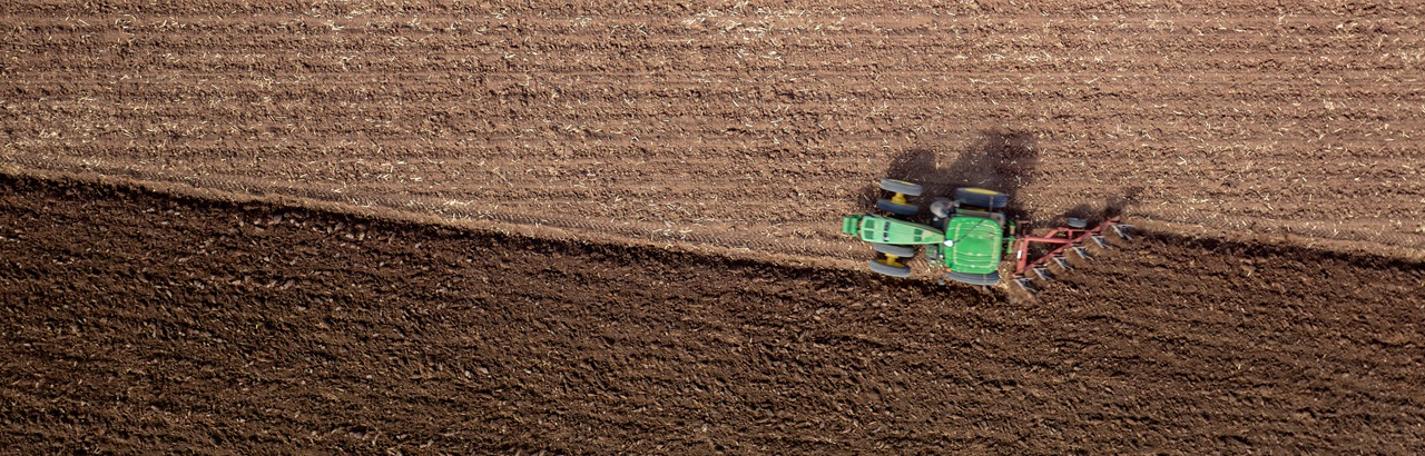 An aerial shot of a tractor driving in a straight line