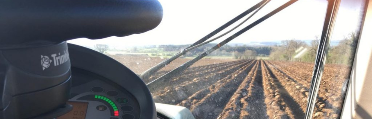 A farmer prepares a field for the season and a Trimble steering system is in the foreground.