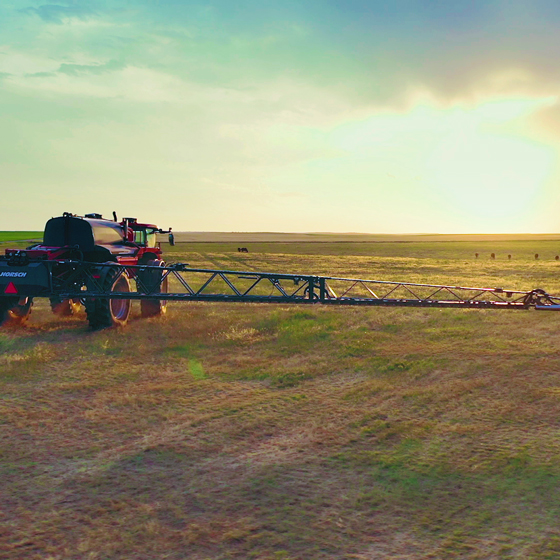 A farmer sprays their field using a HORSCH sprayer at sunset.