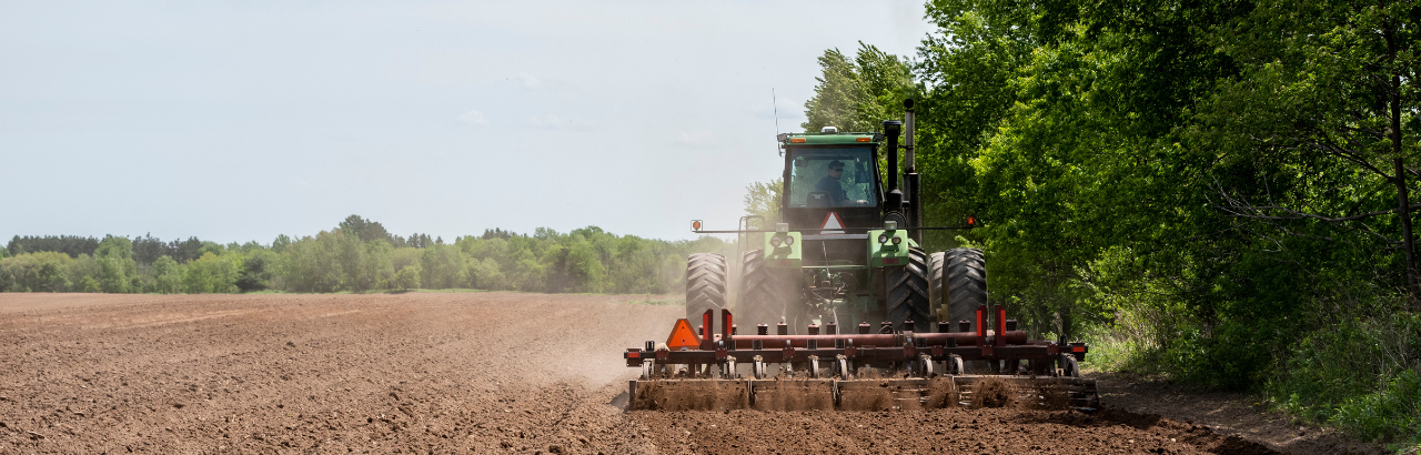A farmer prepares a field for planting along a treeline.