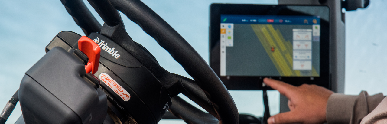 An in-cab photograph of a Trimble steering wheel with a display in the background.