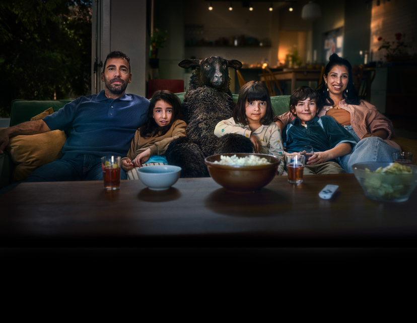 Fåret Frank sitter i soffan med familj och äter popcorn