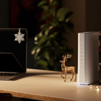 En liten guldfärgad renprydnad på ett skrivbord bredvid en router, böcker och en laptop med snöflingedekor.