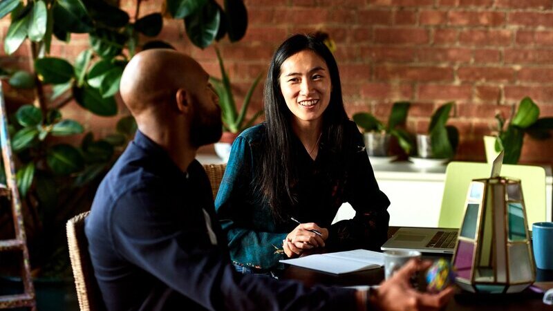 En man och en kvinna samtalar vid ett bord på ett kontor. 