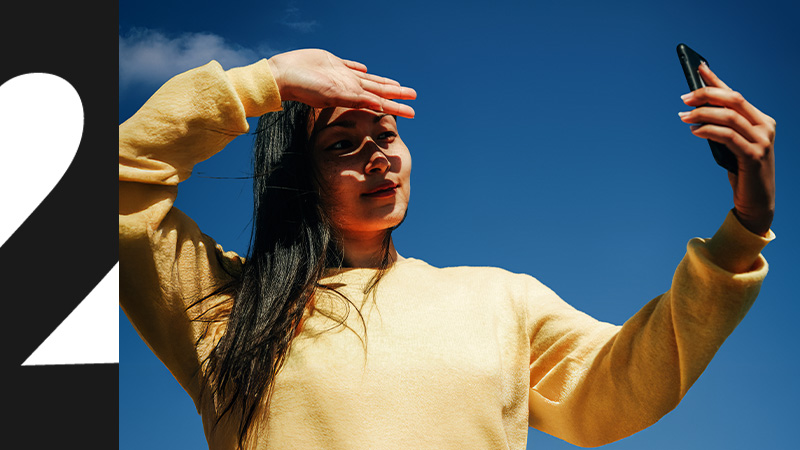 Tjej med mobil i handen mot en blå himmel