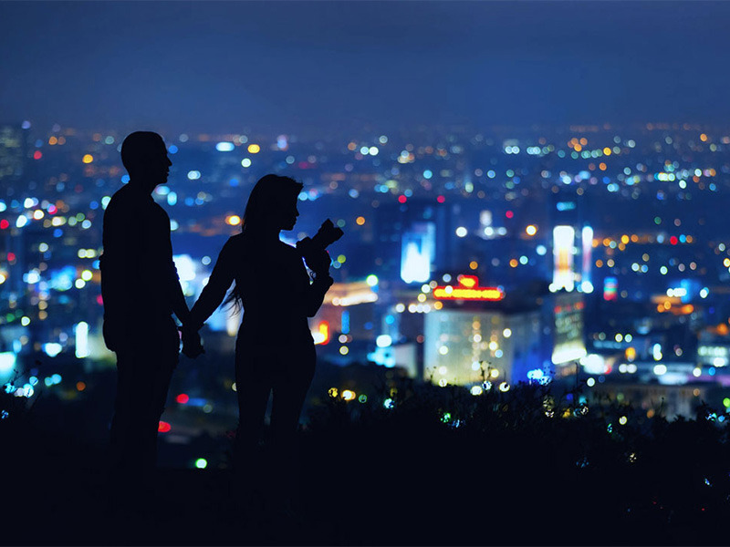 Par som står på en kulle och blickar ut över en stad
