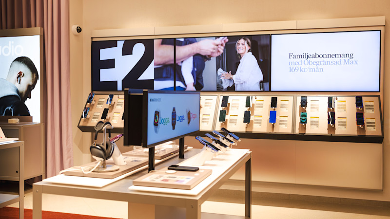 Butiksdisplay från en Tele2-butik med smartklockor och telefoner, digital skärm visar ett aktuellt erbjudande och produktbilder.