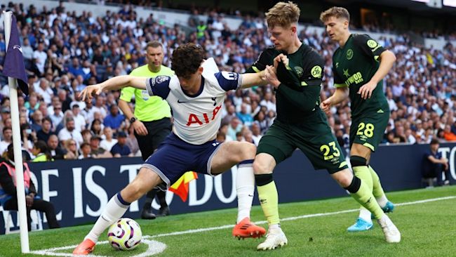 En Tottenhamspelare täcker bollen vid hörnflaggan, attackerad av två spelare i Brentford