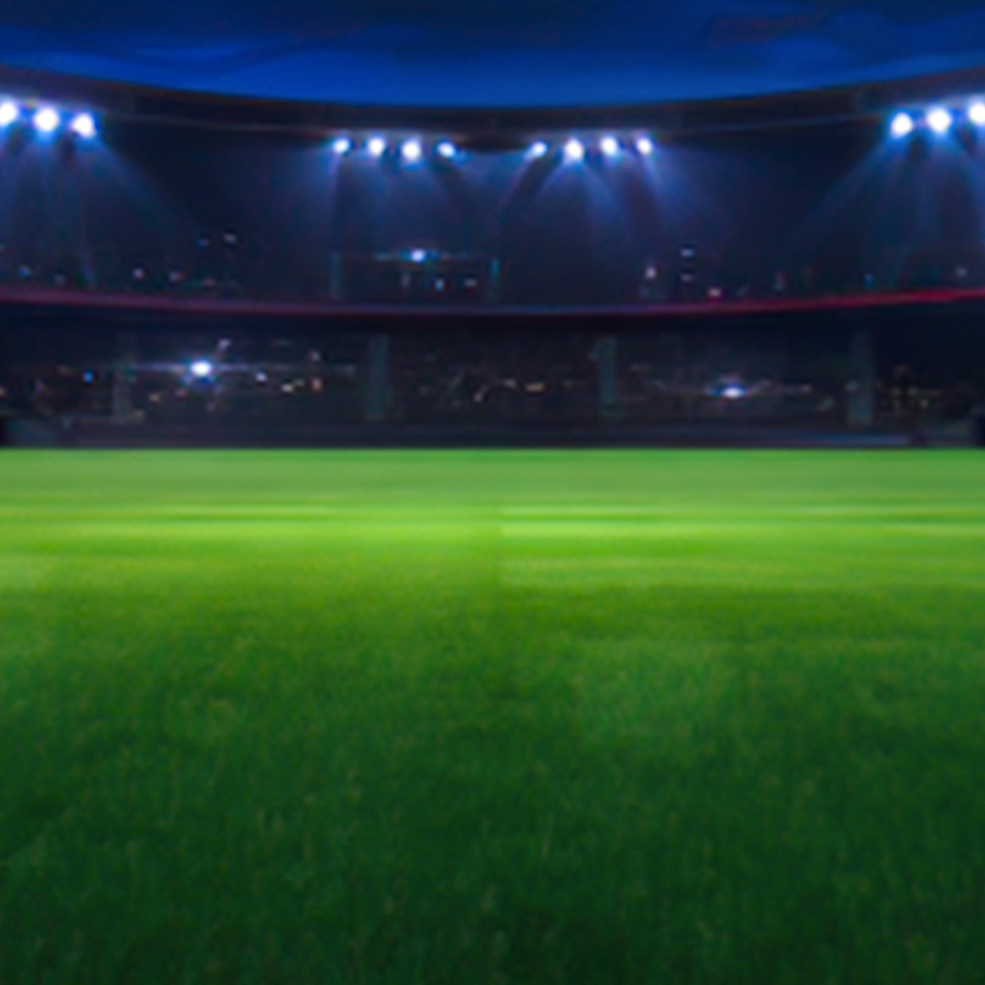 Ett fotbollsstadion på natten med strålkastare som lyser upp den gröna gräsplanen mot en mörk himmel.