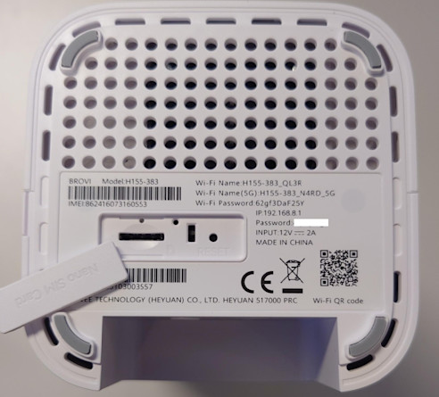 Undersidan av en vit router med ventilationshål, SIM-kortsplats, etikett med modell- och Wi-Fi-information samt QR-kod.