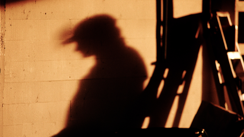 Skuggsilhuett av byggarbetare samt byggmaterial mot orange tegelvägg. 