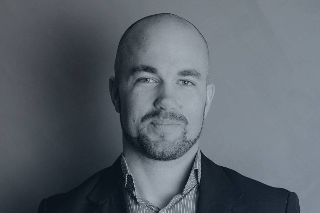 Svartvit bild på Mattias Wiklund, it-chef på Toyota. Han har rakat huvud och kort skägg och är klädd i en randig skjorta och mörk kavaj. Han småler och står vid en grå vägg. 