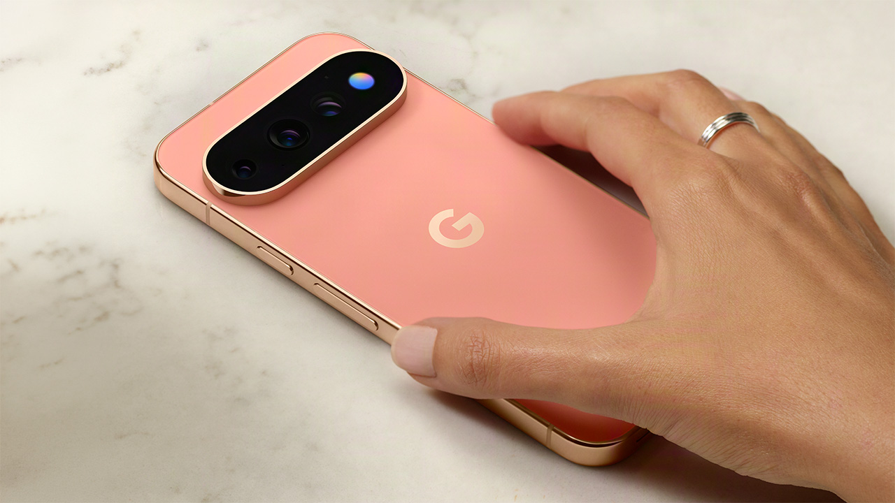 En hand håller en rosa Google Pixel-telefon med trippelkamera på ett marmorbord, sedd bakifrån.