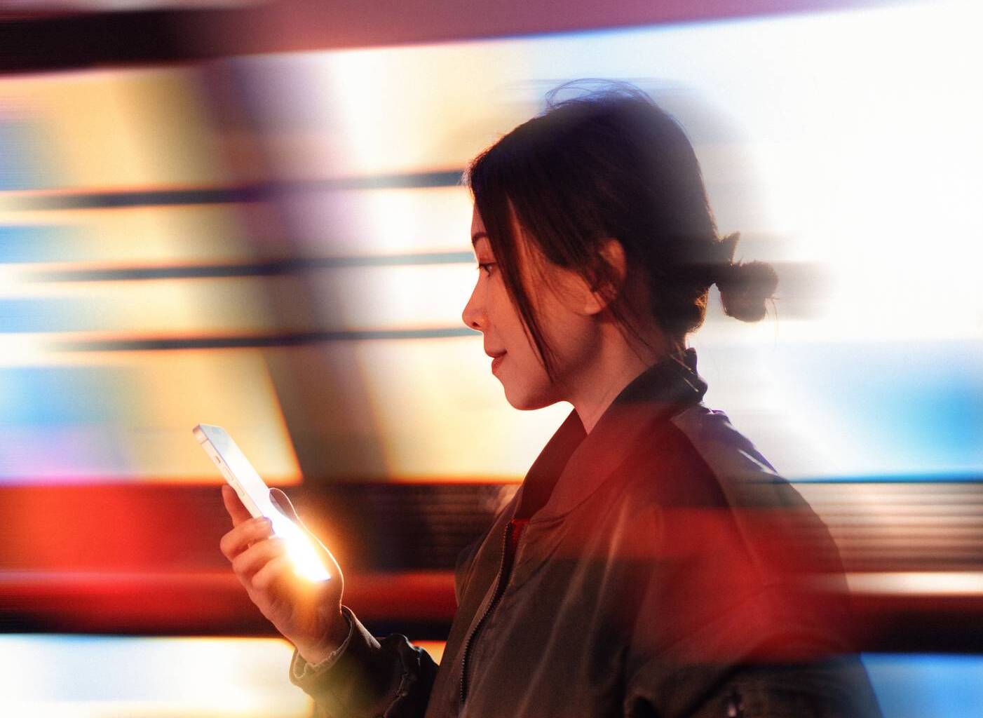 Kvinna håller i en mobil framför abstrakta ränder i olika färger. 