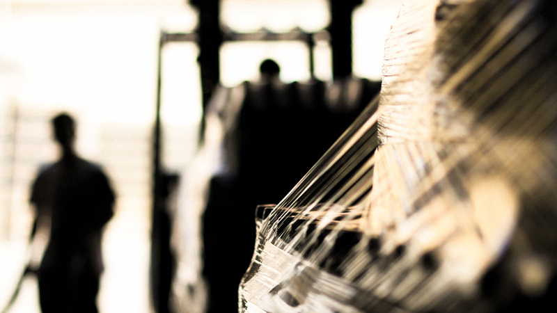 Suddig bild av lagerlokal med lastpallar, lastare samt arbetare i bakgrunden. 