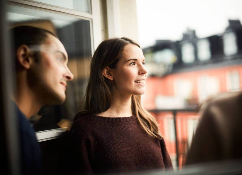En man och en kvinna vid ett öppet fönster med hus i bakgrunden.