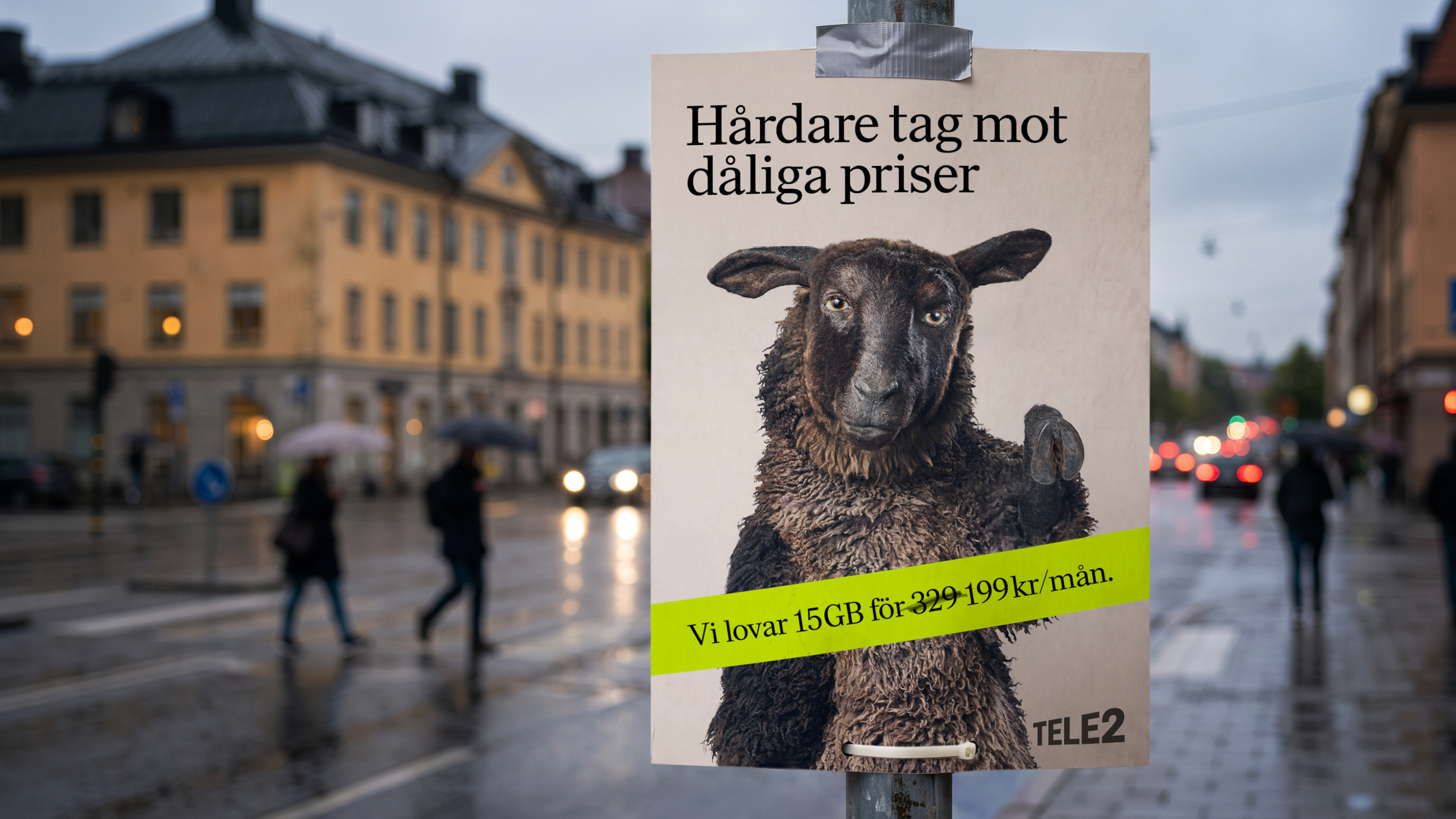 Tele2-affisch på lyktstolpe i regnig stad med ett svart får och texten "Hårdare tag mot dåliga priser, 15GB för 199 kr/mån."
