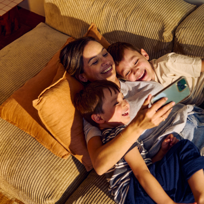 Familj avslappnad i soffa tittar tillsammans på en smartphone i varmt kvällsljus.