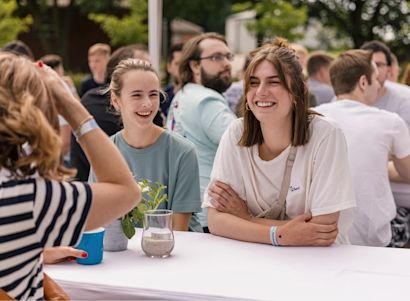 Careers_People_Img People sitting together at an outdoor table during a social event, smiling and chatting.
