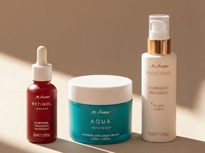 Drei Hautpflegeprodukte auf einer hellen Oberfläche: ein Retinol-Serum mit Pipette, eine blaue Creme und eine weiße Flasche für eine Nachtbehandlung vor neutralem Hintergrund.