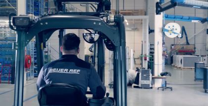 A worker in a forklift with a "Beijer Ref" jacket drives through a warehouse.