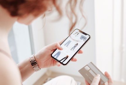 Woman uses a smartphone for online shopping and has a credit card ready. Symbolizes mobile shopping and digital payments.