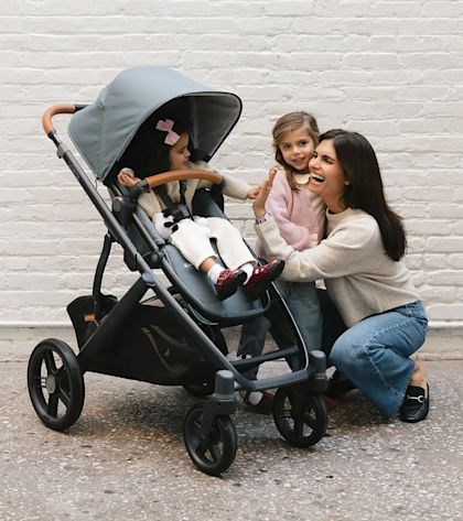 A mother laughing with her two daughters next to an UPPAbaby stroller