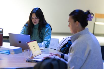 Two female employees are sitting at a table working on their notebooks.