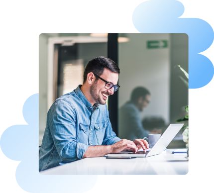 A smiling man with glasses sitting on a laptop