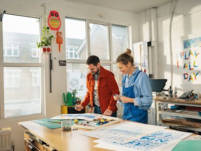 Ein Mann und eine Frau arbeiten gemeinsam an einer Lackierstation und tragen Farbe auf Produkte auf.