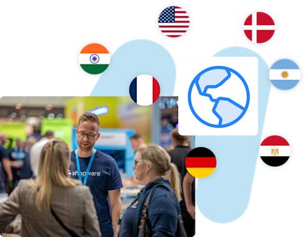 An image showcasing an international event. At the bottom, a person wearing a Shopware t-shirt is talking to two attendees in a expo setting. Above, a globe icon is displayed, surrounded by circular flags representing various countries.