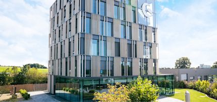Modern multi-story Shopware building with a glass façade, vertical panels, and surrounding greenery on a sunny day.