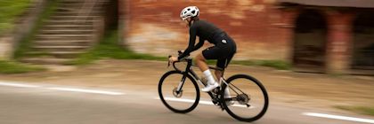 Woman on bicycle wearing black GONSO clothing and white helmet, cycling on a road