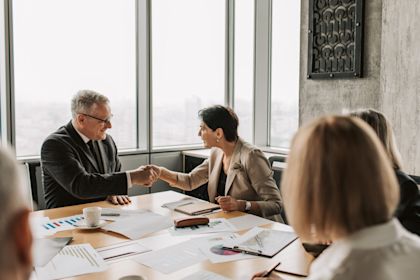 2 people shaking hands in a boardroom over paperwork