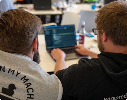 Two developers working together on a laptop with one of them typing.