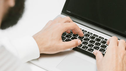 Close-up of hands typing on a laptop keyboard.