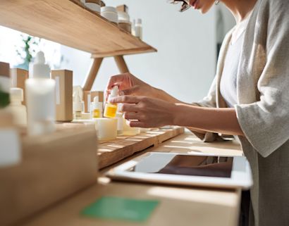 Person arranging skincare products on a workspace beside a tablet, illustrating digital commerce, and product management for beauty and cosmetics.