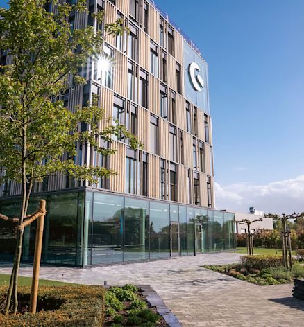 Modern multi-story Shopware building with a glass façade, vertical panels, and surrounding greenery on a sunny day.