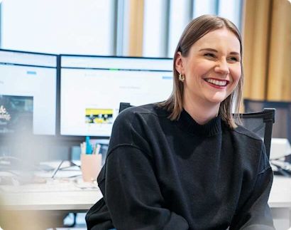 Careers_Design_Hero_Image Women sitting in an office smiling with computer screen in the background.