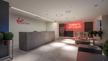 Virgin Active Rome branch reception with "Virgin Active" logo behind a stone desk, and "Screw it, let's do it" neon sign at the entrance