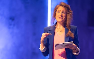 Heike Zellerhoff in a suit on stage moderating the SCD.