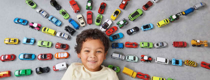 Smiling child laying on the floor with toy cars around him in a 'sunbeam' formation