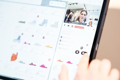 A person browses shoes on a tablet, with product images on the left and a video call on the right. The person’s finger points at an option on the screen.
