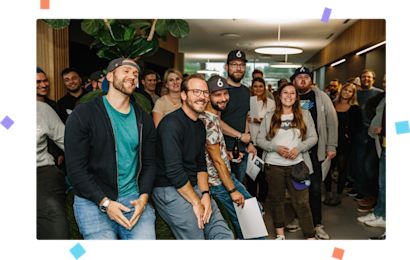 Mitarbeiter Konfetti Shopware Mitarbeiter sind in der Kantine versammelt und lachen zusammen. Das Bild ist von buntem Konfetti umgeben.