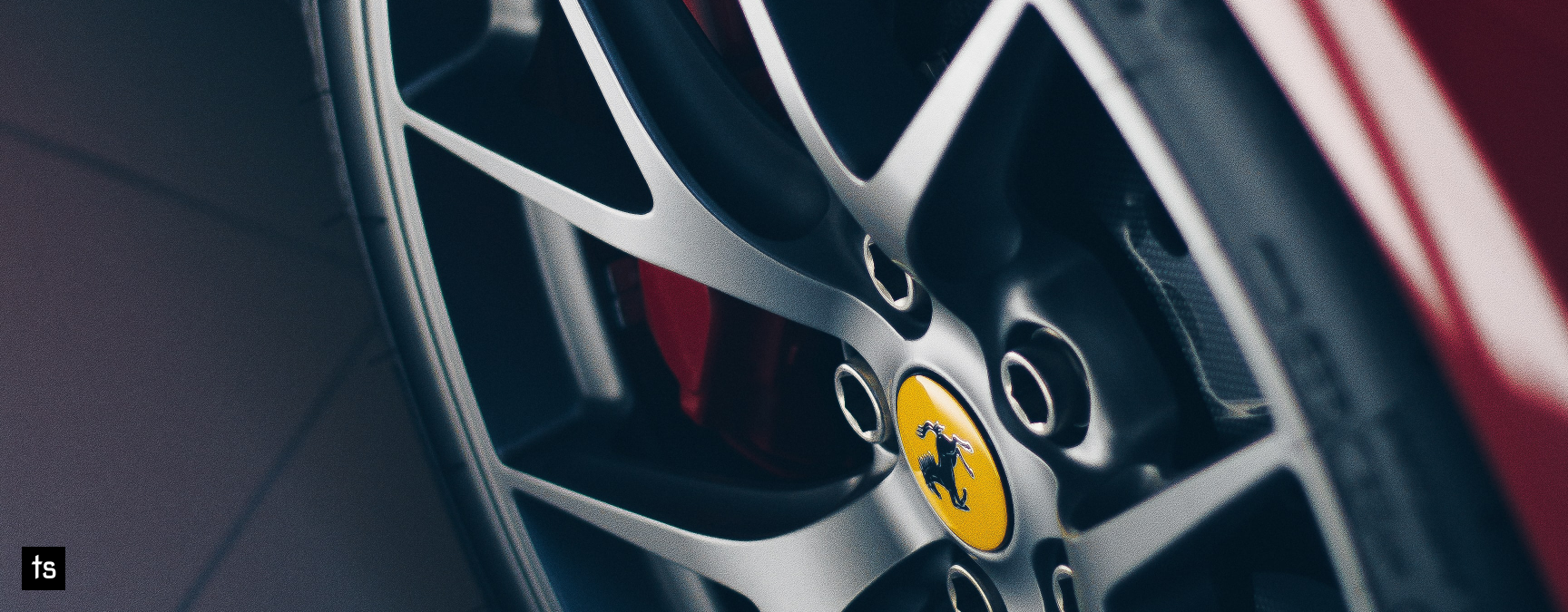 Close-up of a polished alloy wheel on a red Ferrari, featuring the iconic Ferrari logo