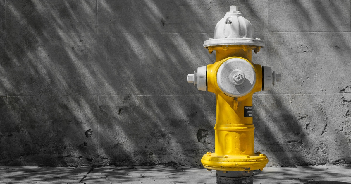 A yellow and white fire hydrant sits on a sidewalk in front of a building. Both the sidewalk and the building are gray.