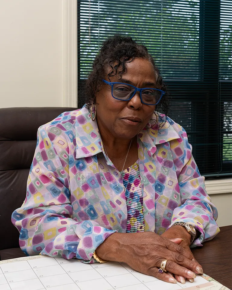 An African American wearing blue glasses and a pastel patterned shirt Dr. Marvel Parker, Executive Director, Emmett Till & Mamie Till-Mobley Institute, sitting at their desk with hands folded.