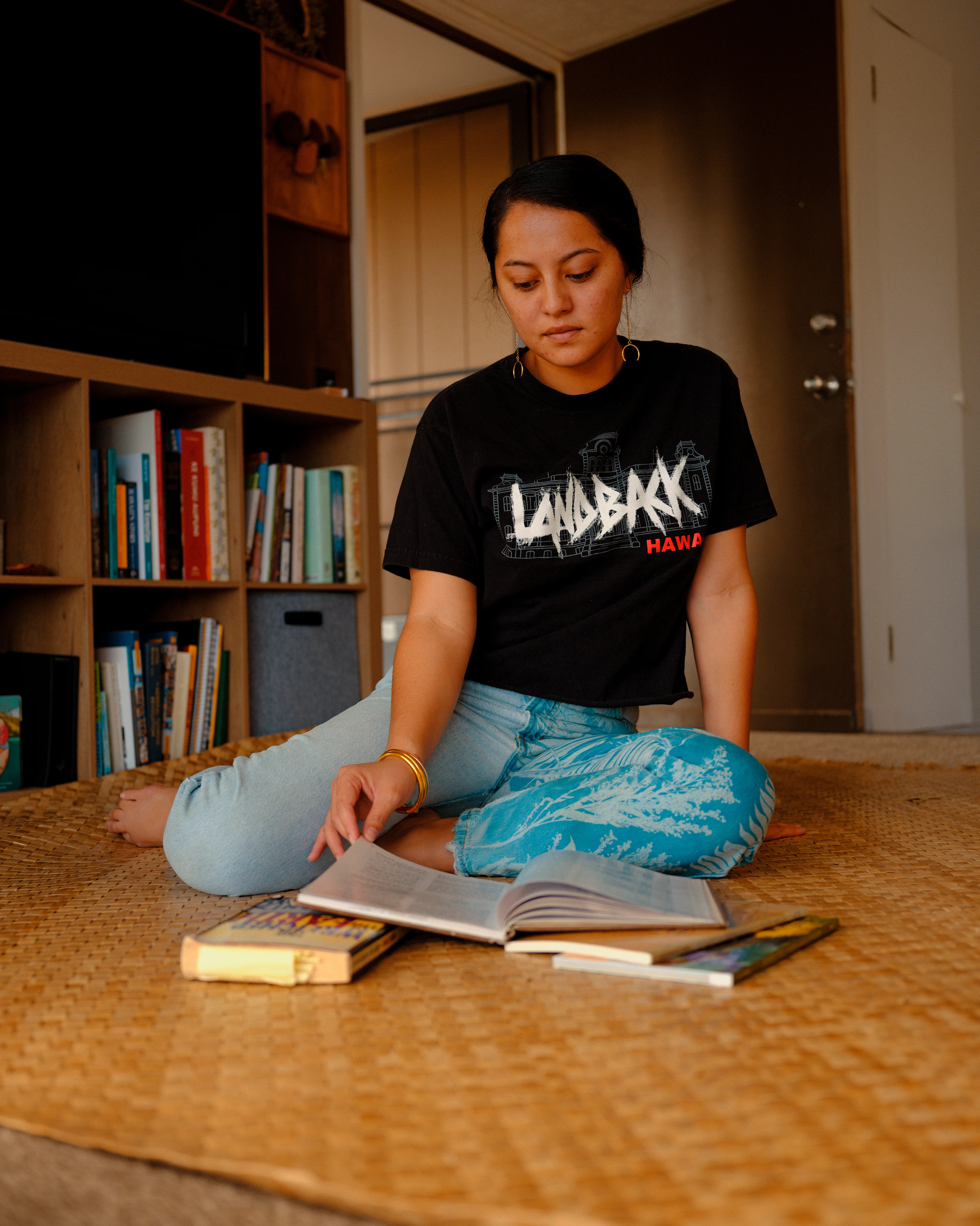 A Pacific Islander college student sits on the floor reading a textbook