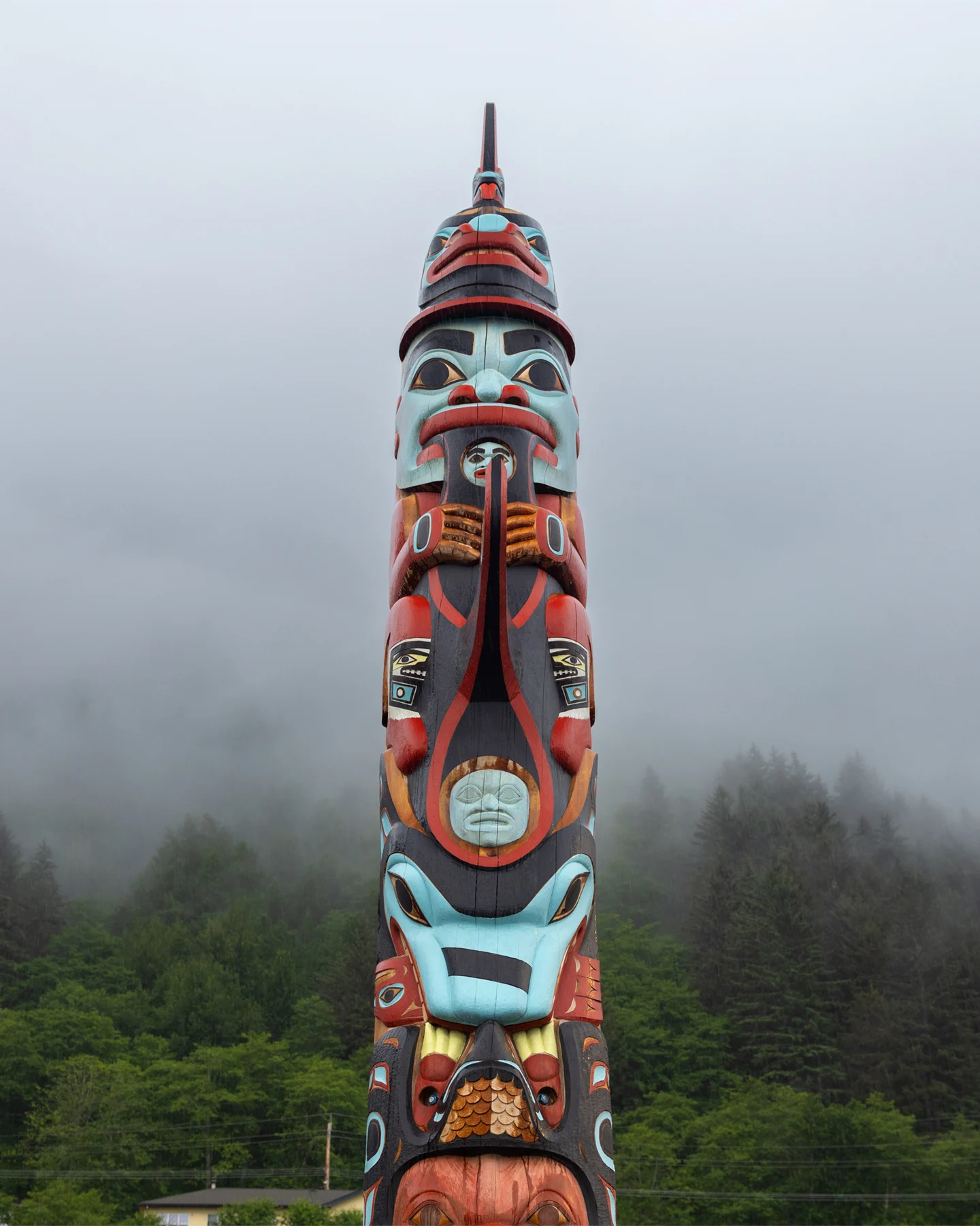A vibrantly painted totem pole set against a backdrop of a foggy forest landscape