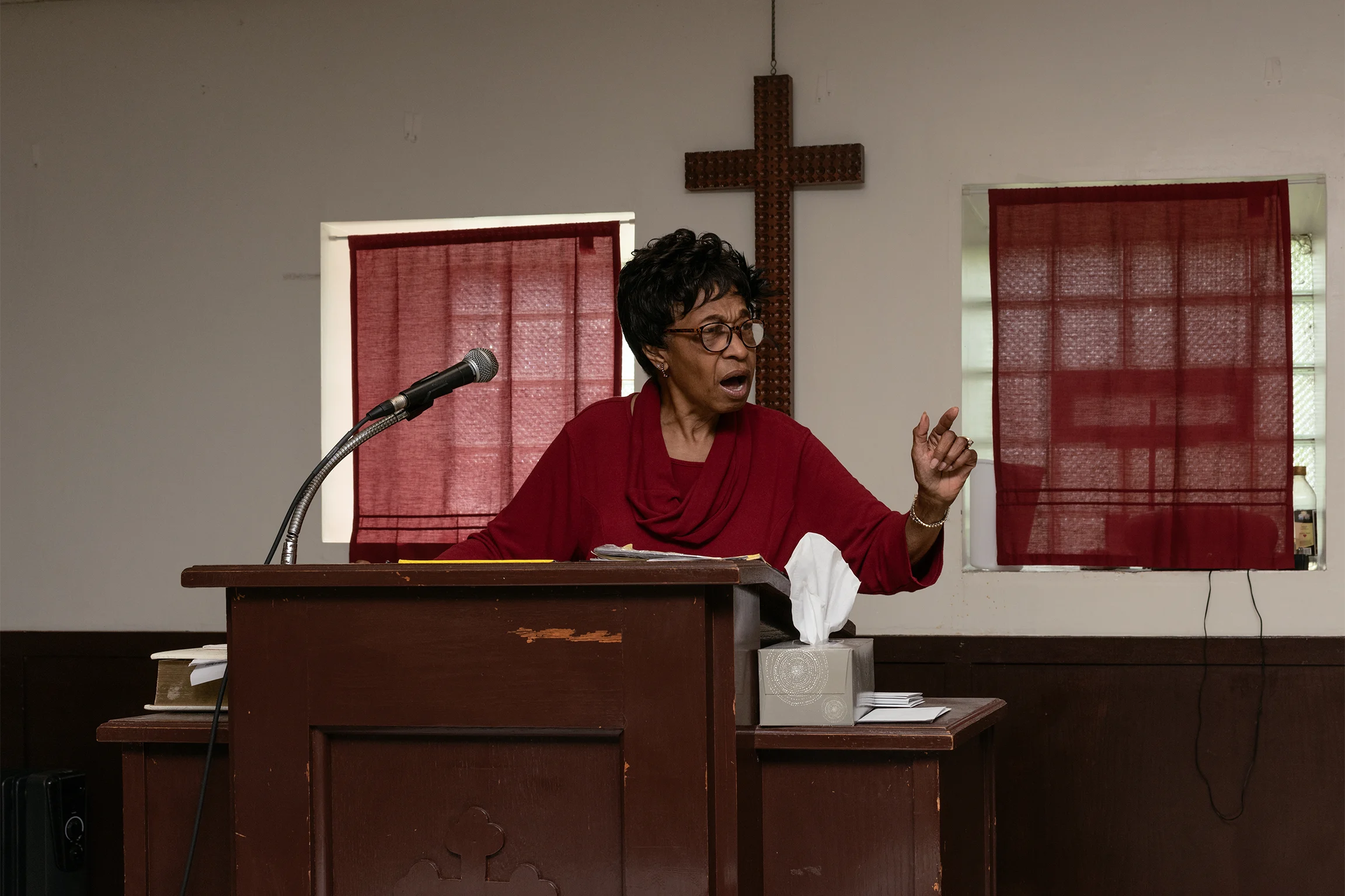 An African American woman dressed in a red top wearing glasses speaks at a podium
